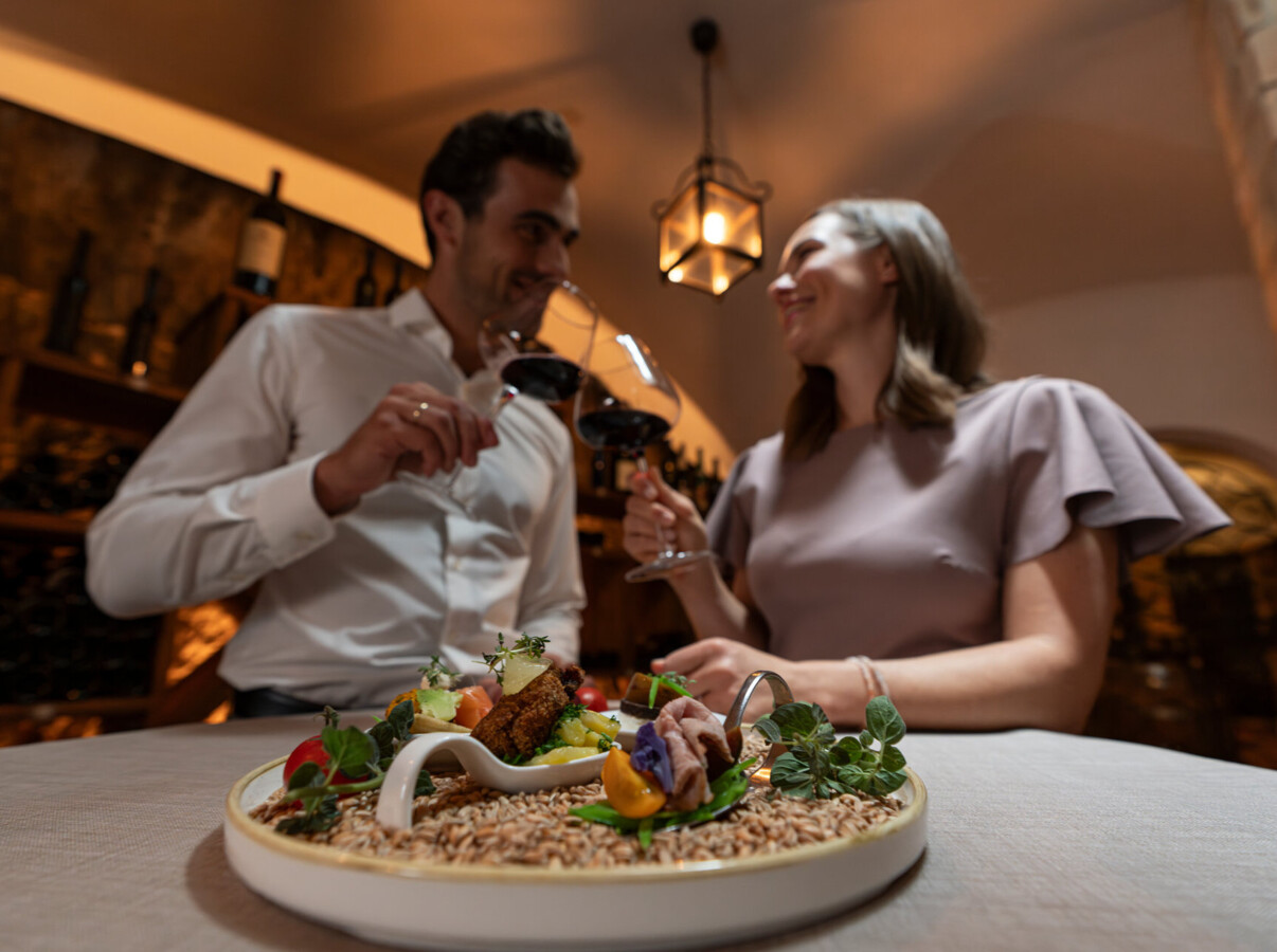 A couple enjoying a gourmet meal with wine in a cozy, elegant setting.