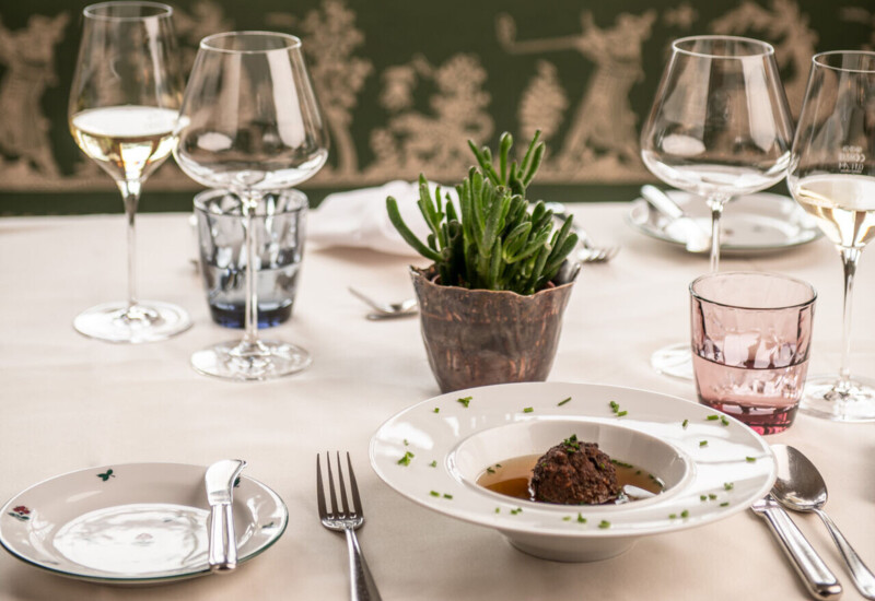 Elegant gedeckter Tisch mit Weingläsern, Pflanzen und einer Speise im Restaurantbereich.