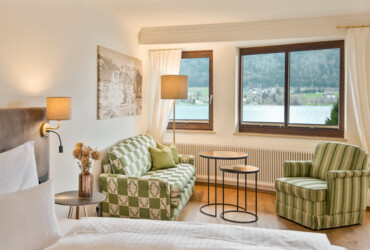 Bright room with patterned furniture, large windows showcasing a lake and mountain view, and a cozy ambiance.