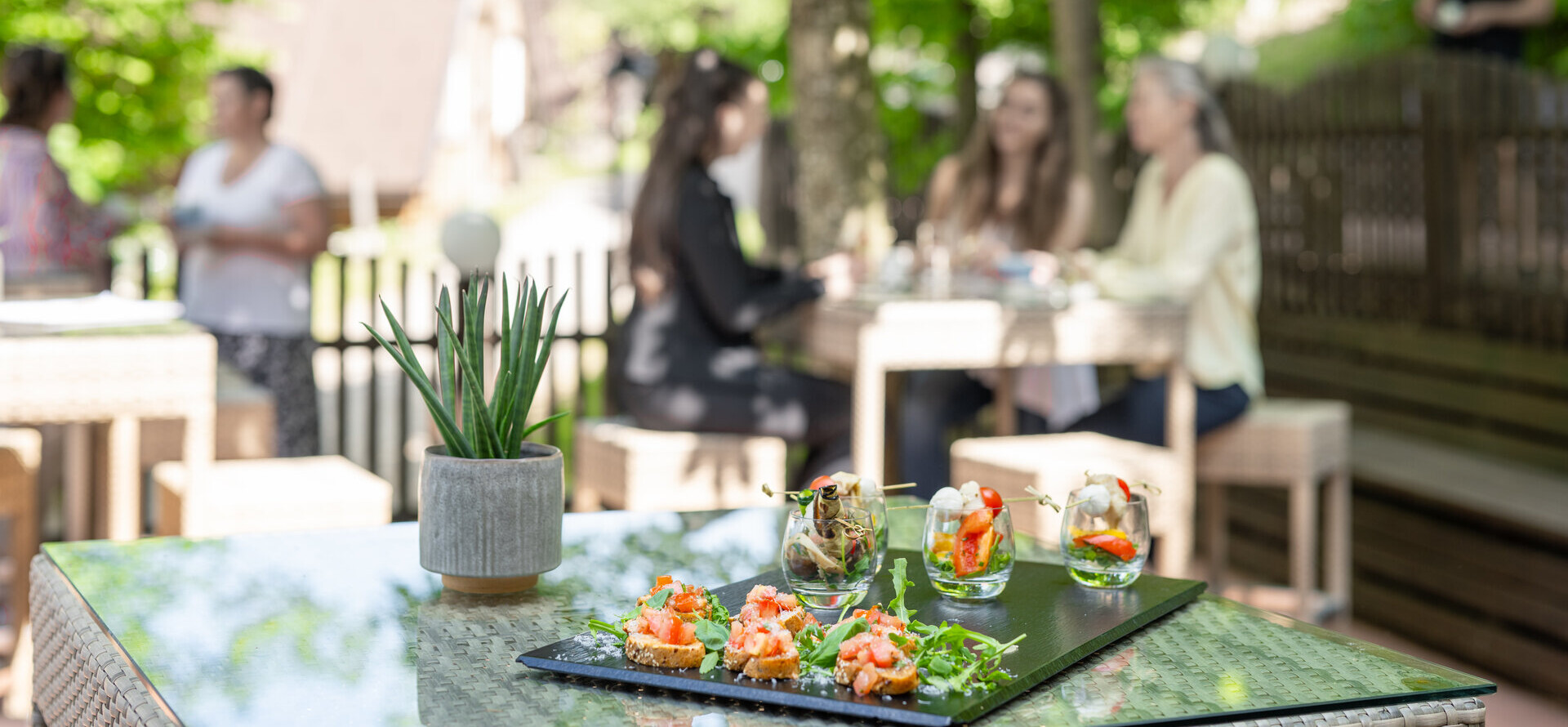 Outdoor dining with gourmet appetizers on a table, surrounded by lush greenery and scenic background. People enjoying a meal in the garden.