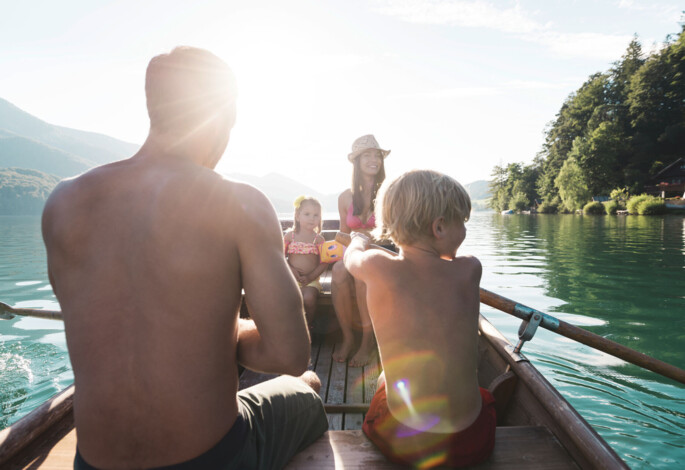 A family enjoys rowing on a serene lake surrounded by lush green forests and scenic mountains.