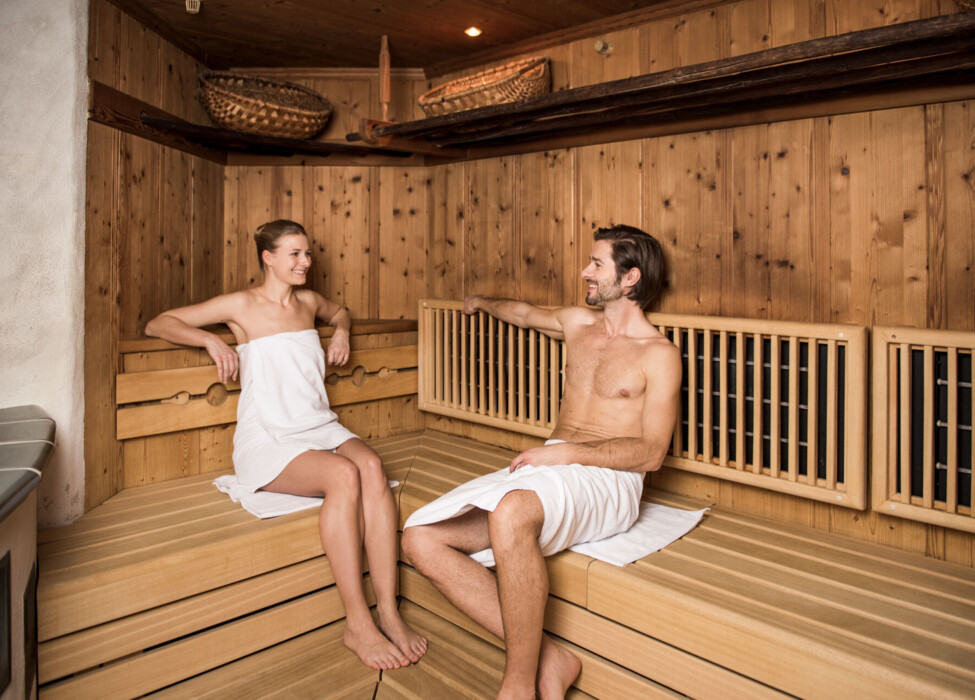 Two people relaxing in a wooden sauna, wrapped in towels.