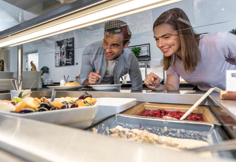 A man and woman eagerly selecting dishes from a breakfast buffet with various colorful food options.