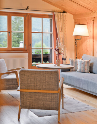 Cozy living room with wooden ceiling, large window, grey armchairs, and a lamp beside a couch.