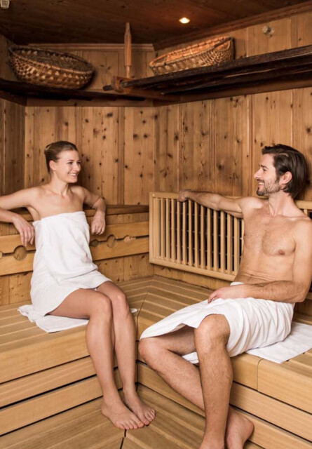 Two people relaxing in a cozy wooden sauna, wrapped in towels.