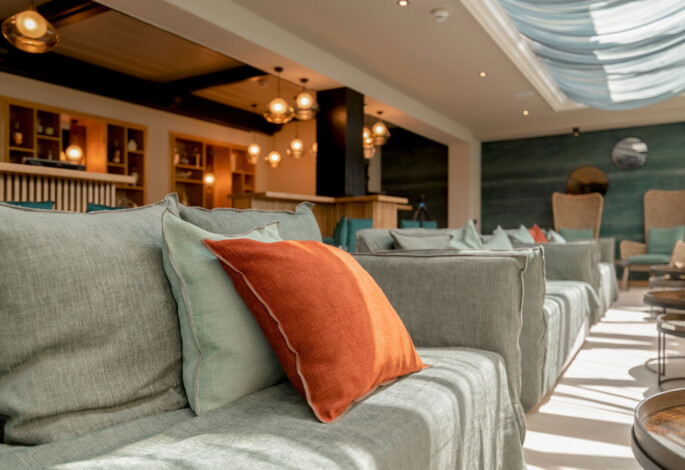 Modern lounge area with soft seating and warm lighting, featuring green and orange cushions.