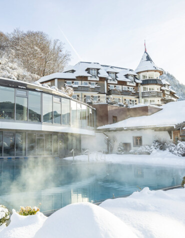 Snow-covered hotel with a steaming outdoor pool, surrounded by winter landscape.