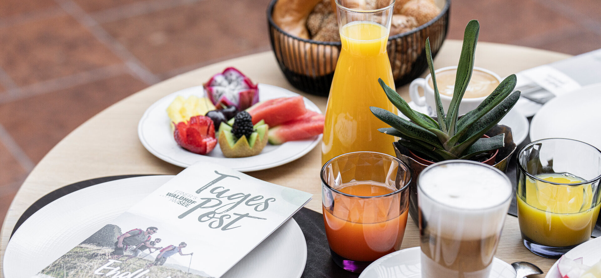 Breakfast table with fruit, juice, coffee, and a brochure titled "Tages Post."