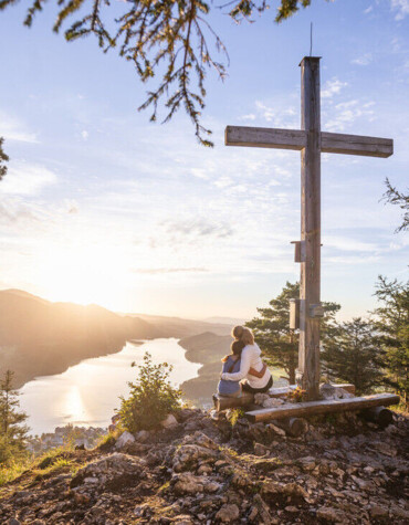 Pärchen vor einem Gipfelkreuz mit Blick auf en Fuschlsee.