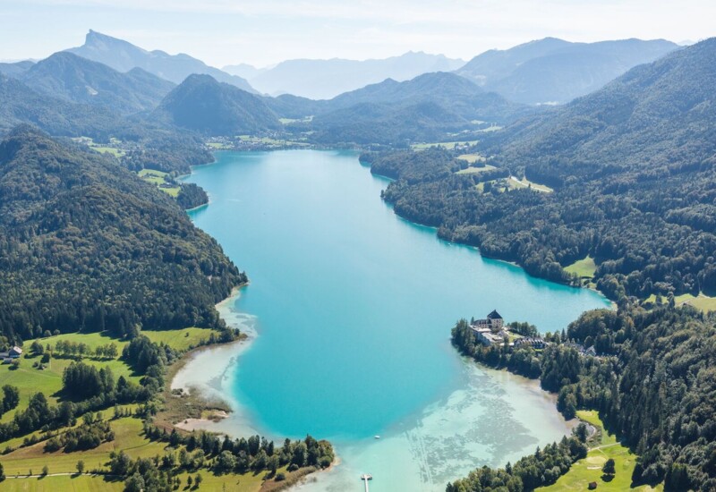 Aerial view of a scenic, lush landscape with a tranquil blue lake surrounded by green hills and mountains.