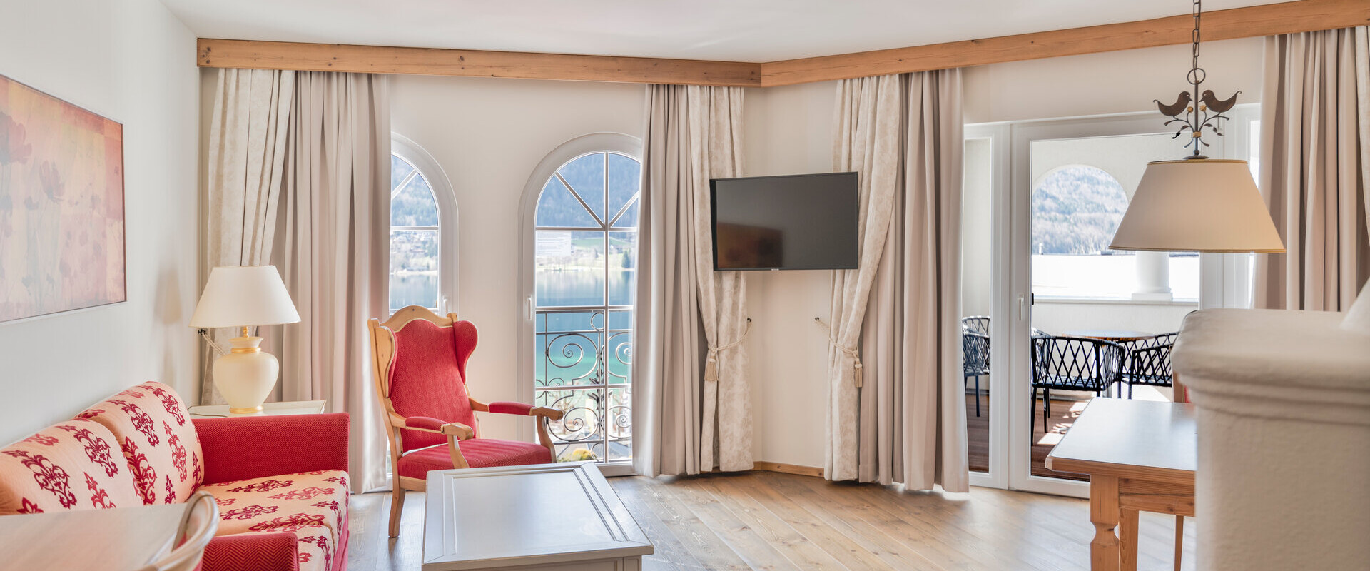 Hotel room with elegant furniture, arched windows, and a view of the lake Fuschl.