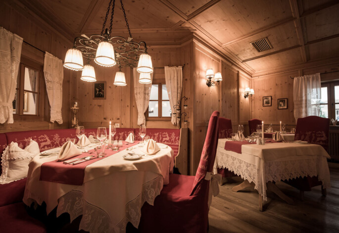 A cozy, elegantly set dining room with wooden interiors, soft lighting, and neatly arranged tables with red and white linens.