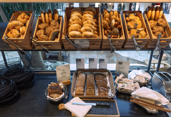Frühstücksbuffet mit einer Auswahl an frischen Brötchen und Brotscheiben in Körben, Servietten, einem Toaster und Butterpäckchen.