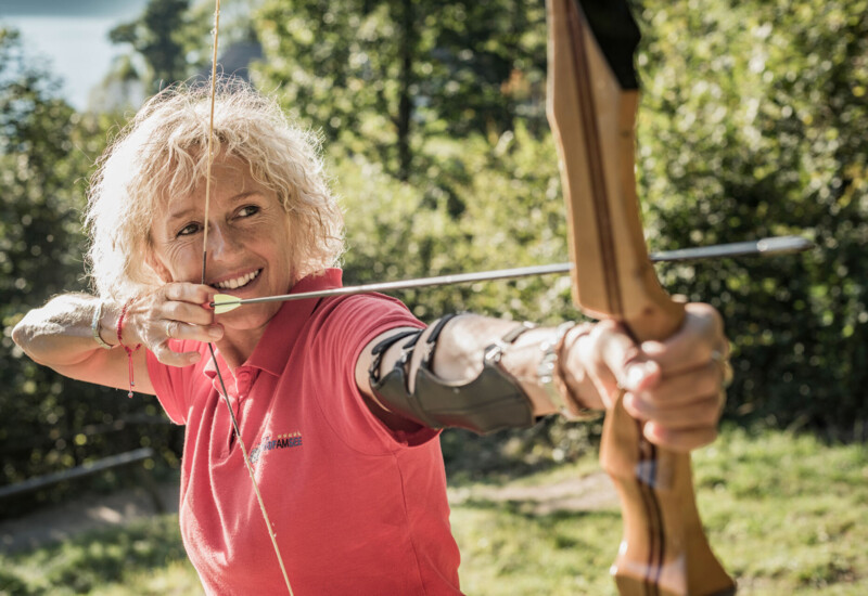 A person enjoying archery outdoors, aiming a bow in a scenic, lush setting.