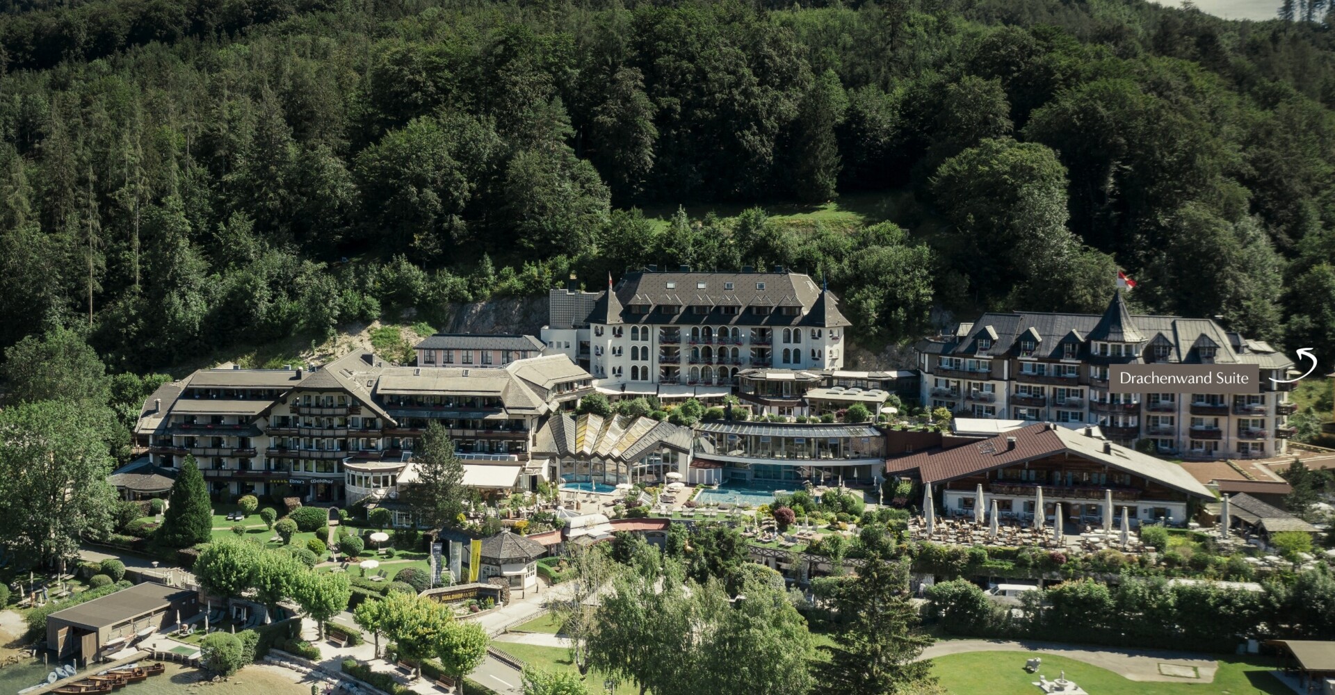 Aerial view of a scenic hotel nestled among lush greenery with lake access.