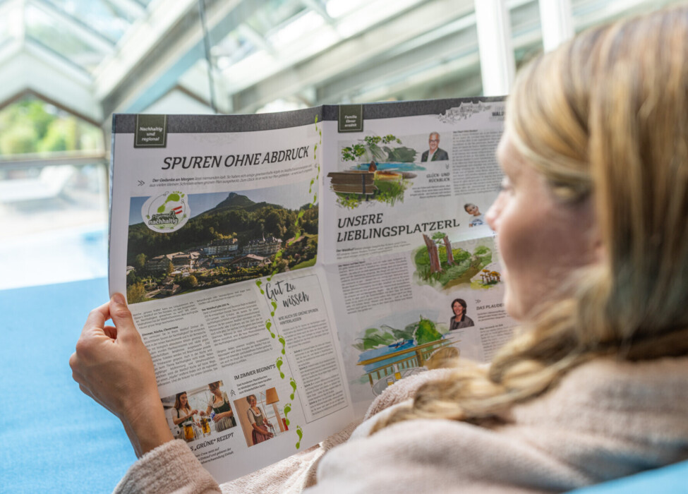 A person reading a magazine featuring scenic landscapes and sustainability topics indoors.