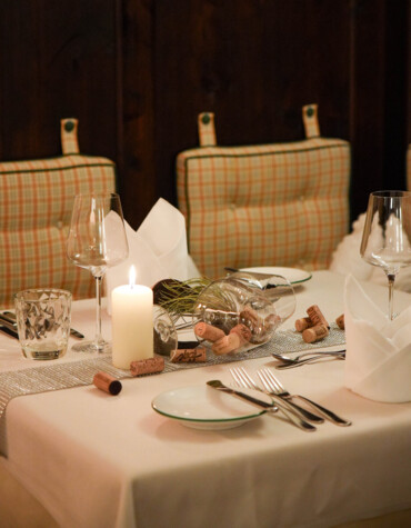 Elegant dining table set with glassware, a lit candle, and wine corks on a white tablecloth.