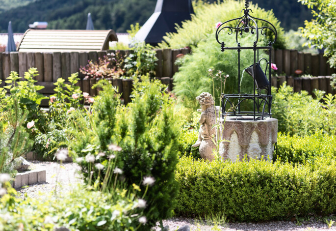 A lush garden with a scenic view, featuring a decorative stone well and greenery.