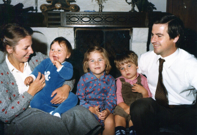 Family Ebner sits together by a fireplace, smiling and enjoying each other's company.