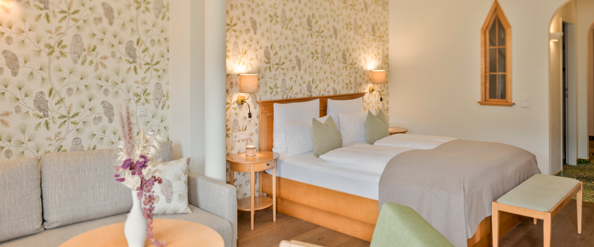 Hotel room with floral wallpaper, a double bed, sofa, and armchair.