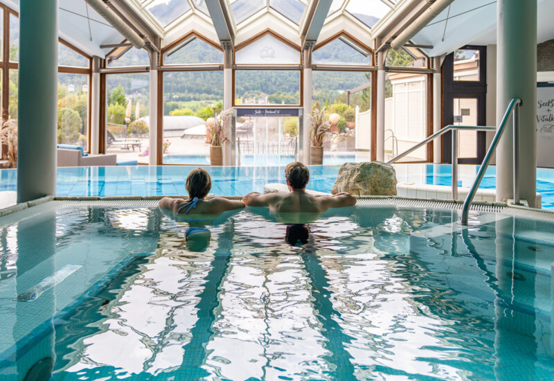 Ein Paar entspannt im Innenpool mit Panoramablick auf die Berge im Hintergrund.