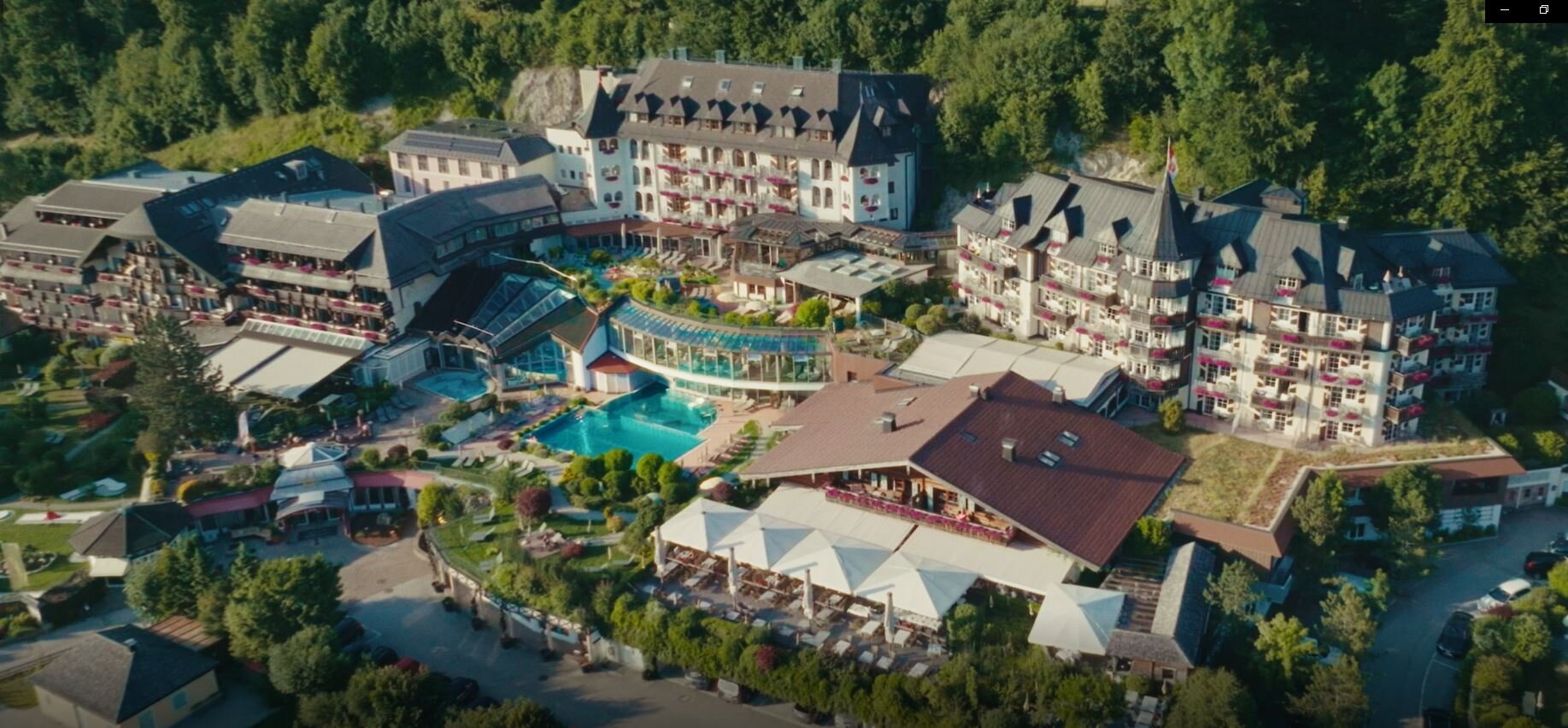 Aerial view of Waldhof Fuschlsee Resort with multiple buildings, a pool, and surrounding greenery.