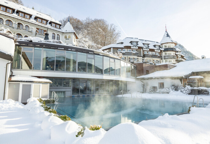 Snow-covered hotel with a steaming outdoor pool, surrounded by winter landscape.