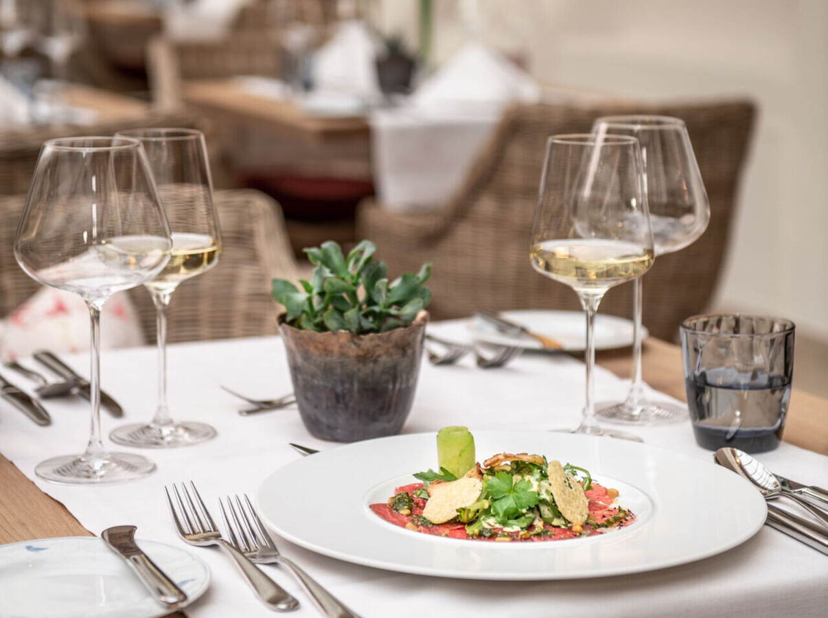 Elegant restaurant table setting with a gourmet dish, wine glasses, and a small plant.