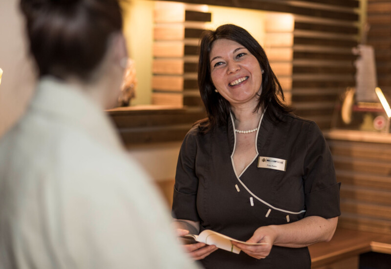 A smiling staff member at a reception desk, engaging with a guest.