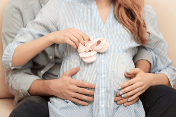 Ein Paar hält Baby-Schuhe auf dem Bauch der schwangeren Frau.