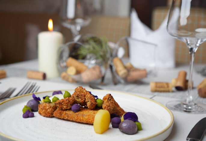 Gourmet dish with colorful vegetables on an elegant table setting, featuring a lit candle and wine corks in the background.