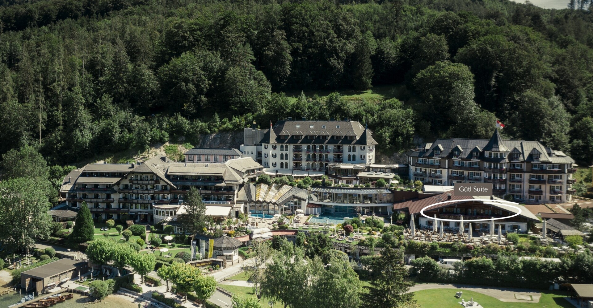 Aerial view of a scenic hotel surrounded by lush greenery near a lake.