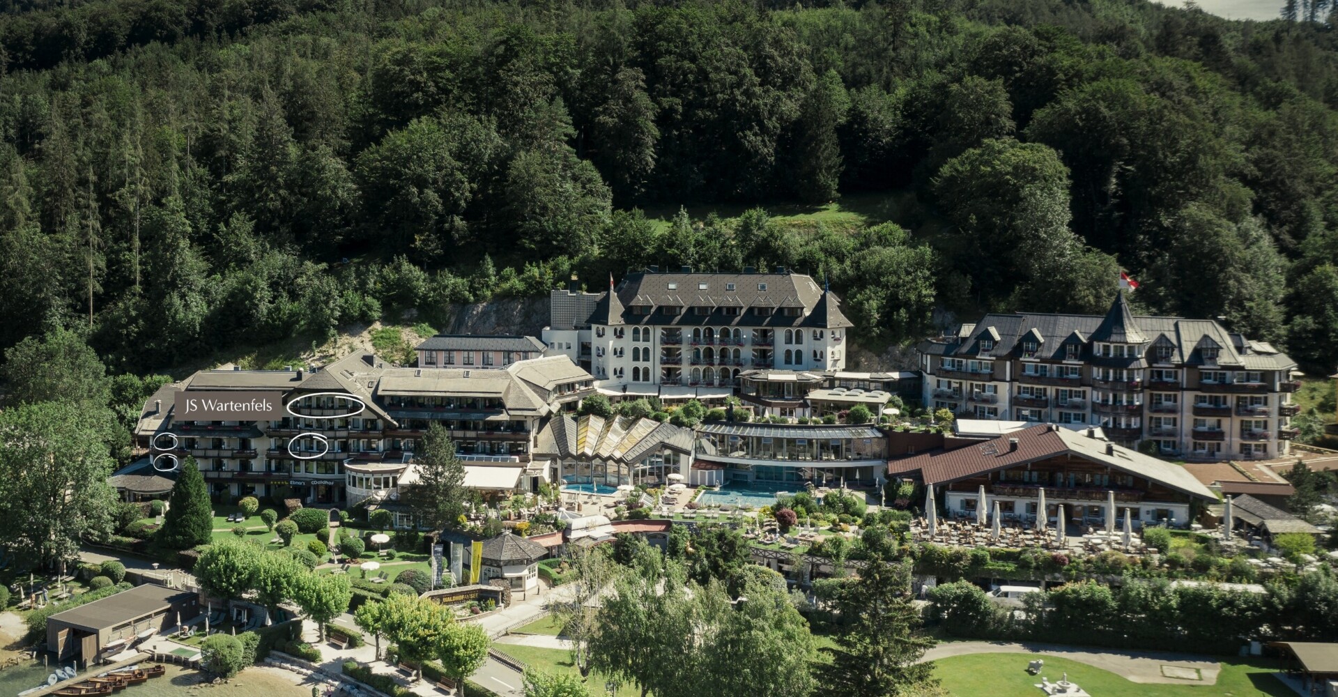 Aerial view of Waldhof Fuschlsee Resort surrounded by trees, with a lakeside beach and garden areas.