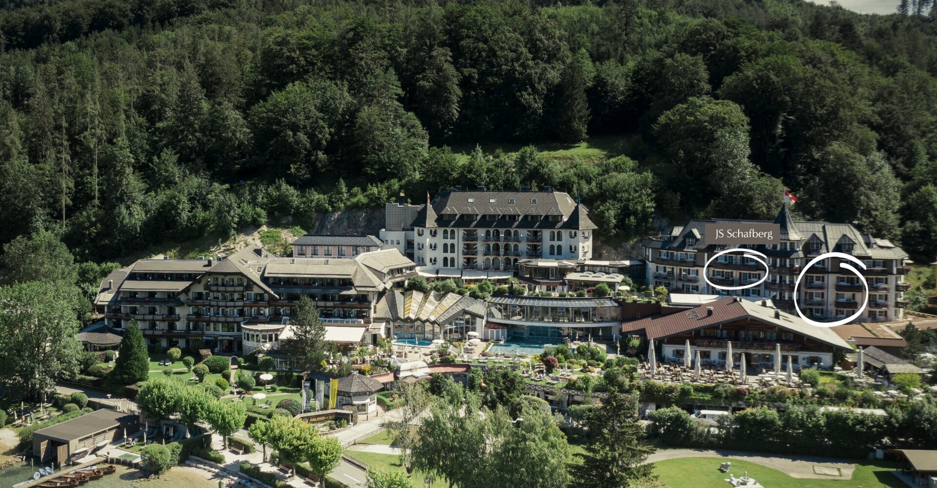 Aerial view of a hotel complex surrounded by lush greenery and scenic landscapes near a lake.