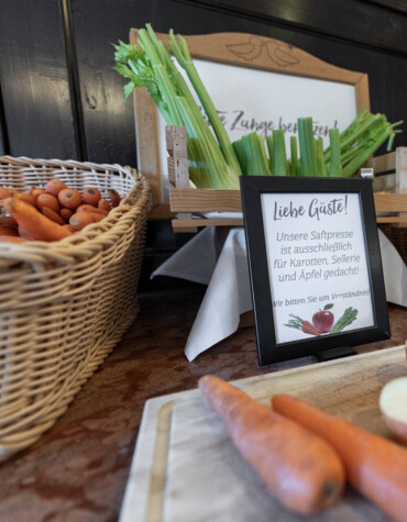 Fresh juice station with baskets of carrots, celery, apples, and a juicer. A sign requests these ingredients only for juicing.