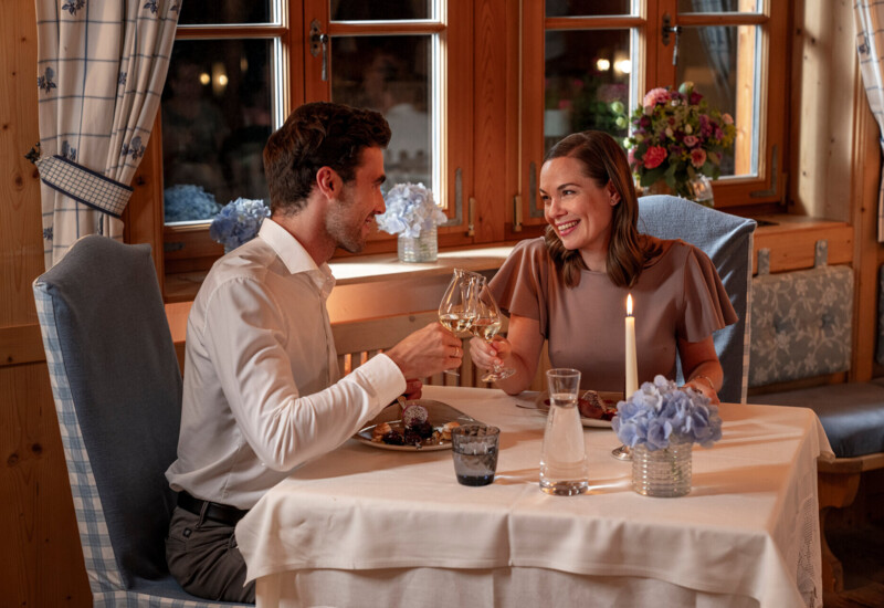 A couple enjoying a romantic dinner in a cozy, elegantly decorated restaurant with flowers and candlelight.
