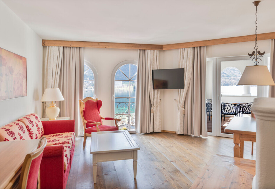 Hotel room with red furniture, wooden floors, and large windows overlooking a scenic view.