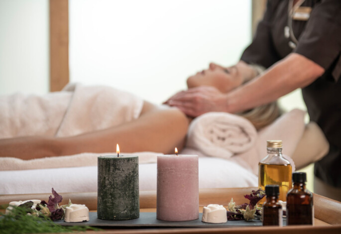 A woman enjoys a relaxing massage with candles and essential oils nearby, creating a tranquil spa atmosphere.