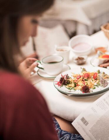 A person enjoys breakfast with a newspaper, featuring a plate of scrambled eggs and a variety of foods on a table.