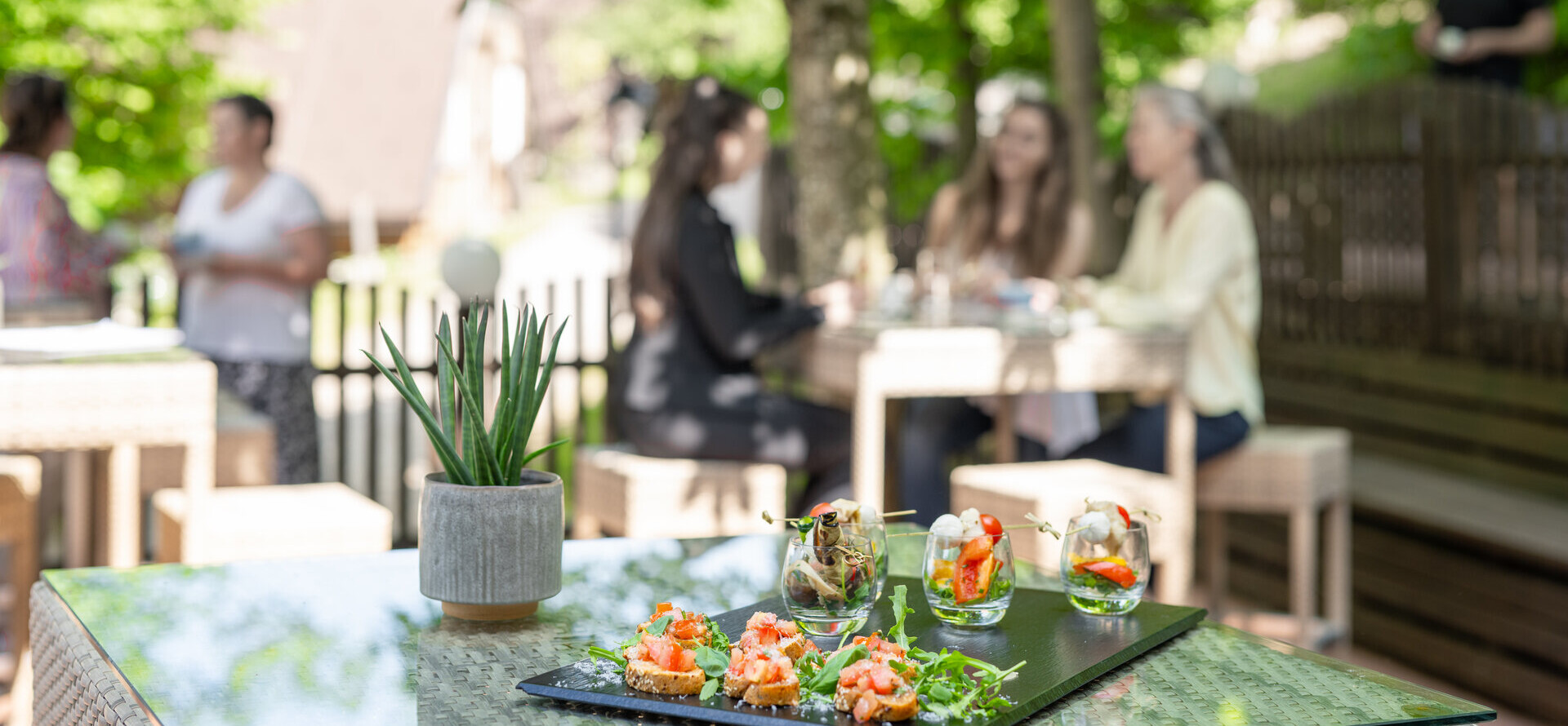 Gemütliche Terrasse mit Speisen und Menschen im Hintergrund, umgeben von grüner Natur am Fuschlsee.