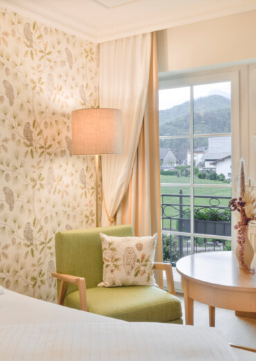 Cozy hotel room with floral wallpaper and a view of scenic mountains through a window.