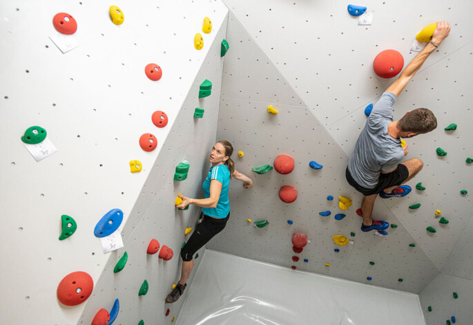 Two people rock climbing indoors on a wall with colorful holds.