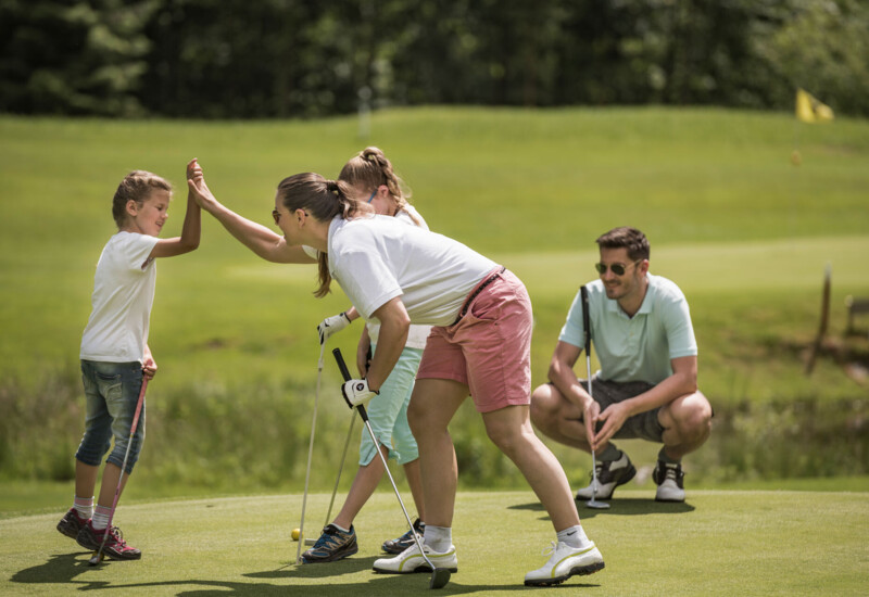 A family enjoying a game of golf on a lush, scenic course, with a child and adult sharing a high-five.