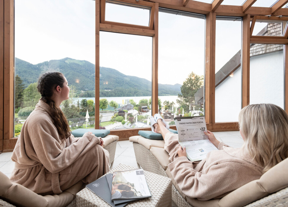 Zwei Freundinnen genießen den Ausblick aus den Panoramafenstern im Ruhebereich des Wellnesshotel Ebner's Waldhof am See.