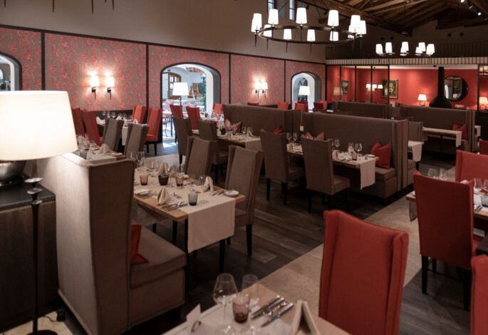 Elegant restaurant interior with red and beige seating, set tables, and soft lighting.