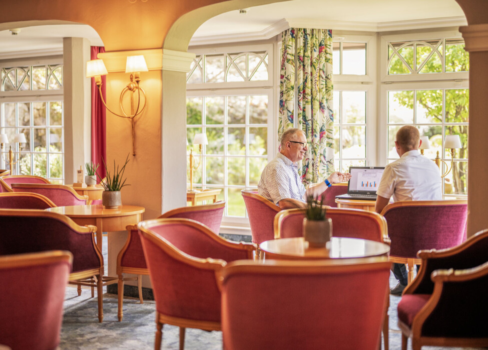 Two people having a meeting in a bright, cozy room with large windows and elegant decor.