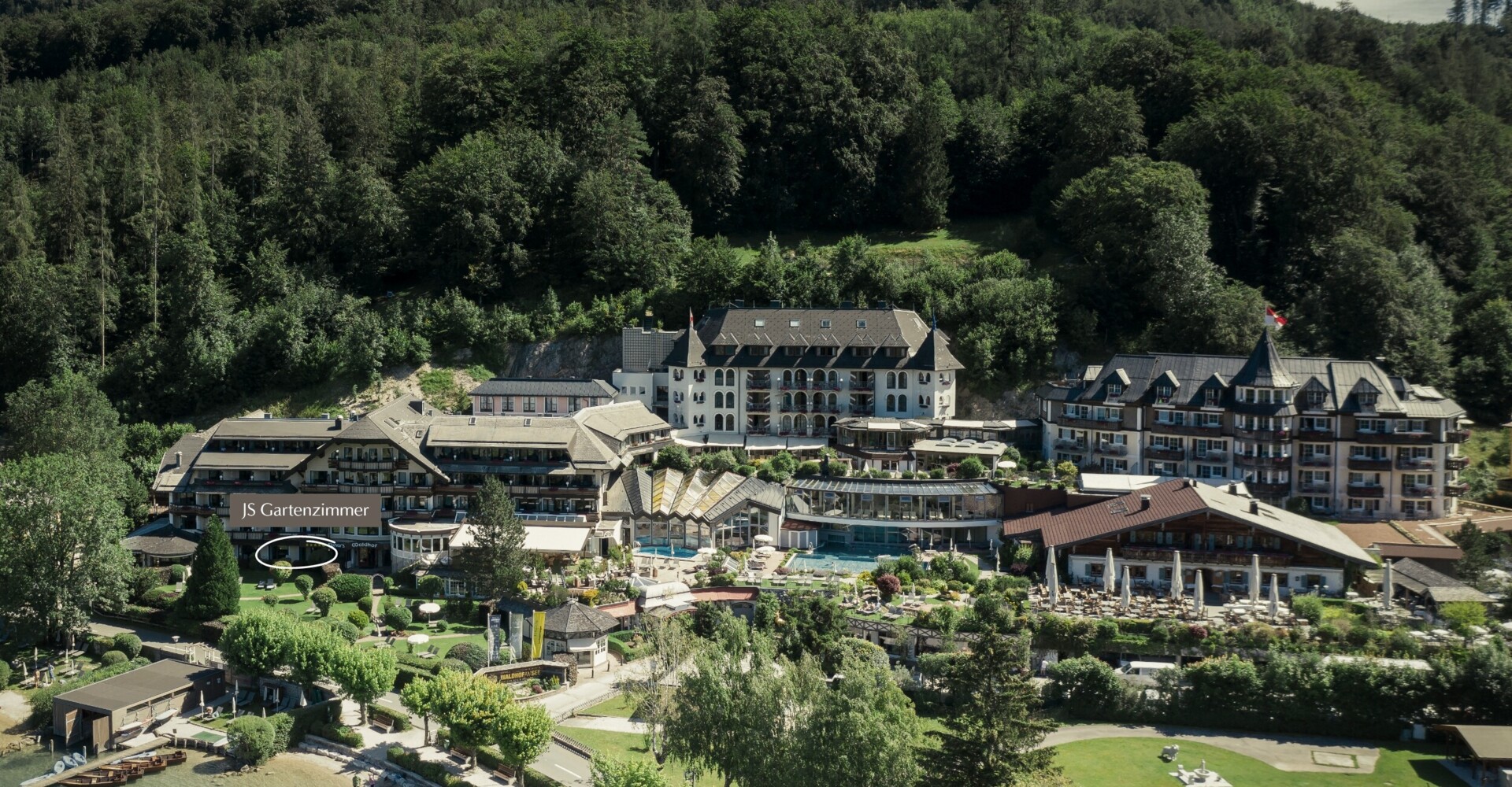 Aerial view of a scenic hotel surrounded by lush greenery near a lakeside.