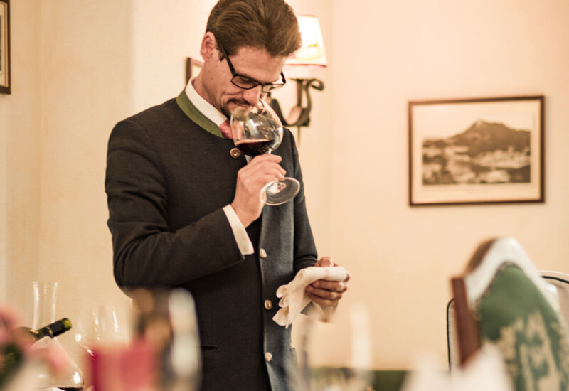 A person tasting wine in a cozy, elegant dining setting with soft lighting and framed art on the walls.