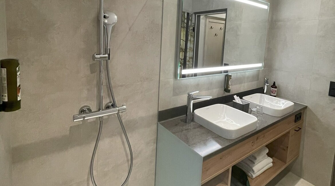 Modernes Badezimmer mit Regendusche, beleuchtetem Spiegel und Doppelwaschbecken auf einer stilvollen Waschtischplatte.