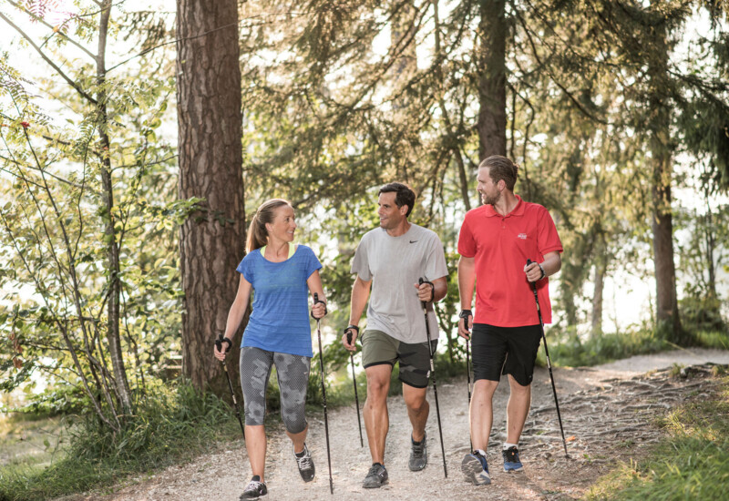 Drei Personen beim Nordic Walking im Wald am Fuschlsee, umgeben von Bäumen und Natur.